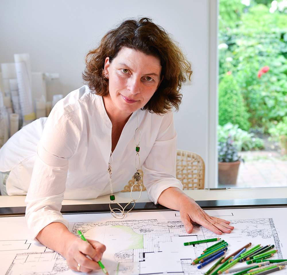 Eine Frau, die an einem Tisch mit einem Zeichenblock und Bleistiften eine Blaupause anfertigt.