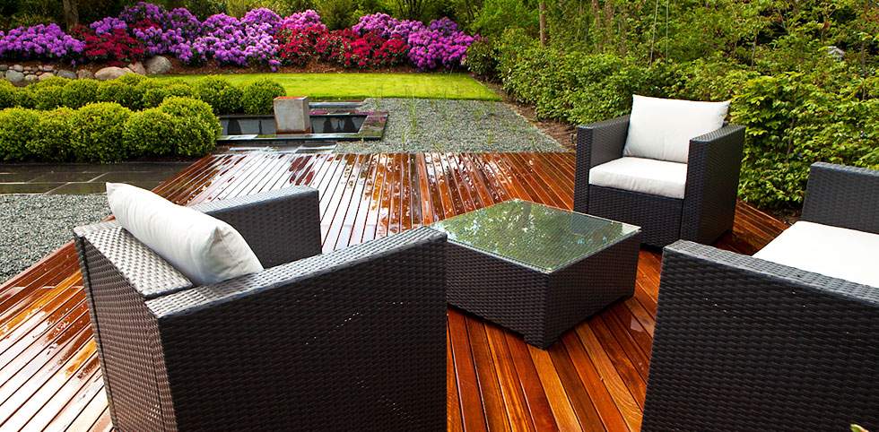 Holzterrasse mit Korbmöbeln und blühenden Blumen.