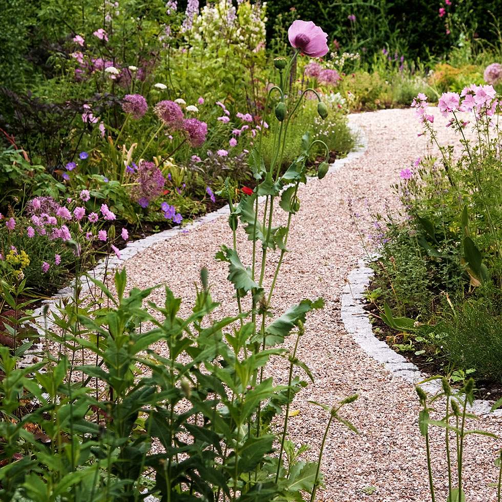 Ein Kiesweg führt zu einem Garten voller bunter Blumen.
